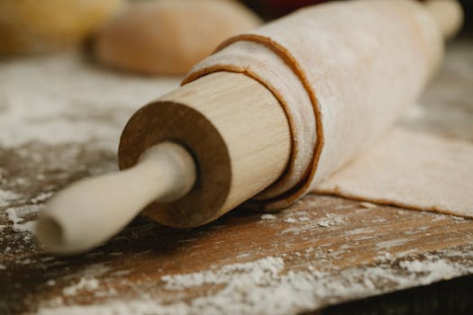 Close-up of a wooden rolling pin with fresh dough in a rustic kitchen setting.