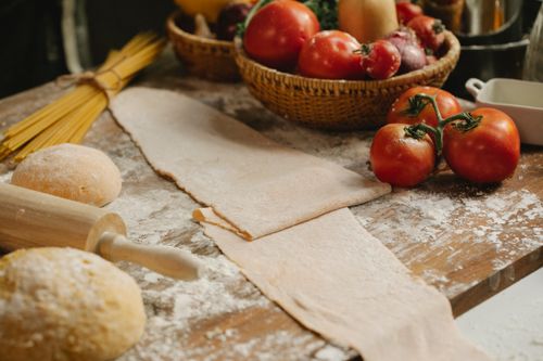 Free Layer of rolled dough placed on messy wooden table sprinkled with flour near ripe tomatoes and raw spaghetti in kitchen Stock Photo