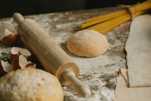 Free Uncooked balls of dough near rolling pin placed on wooden table sprinkled with flour with eggshell and raw spaghetti in kitchen Stock Photo