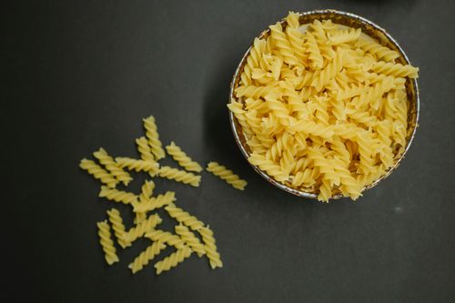 Free Top view pile of uncooked fusilli pasta twisted into springs in bowl and scattered macaroni placed on black background in kitchen Stock Photo