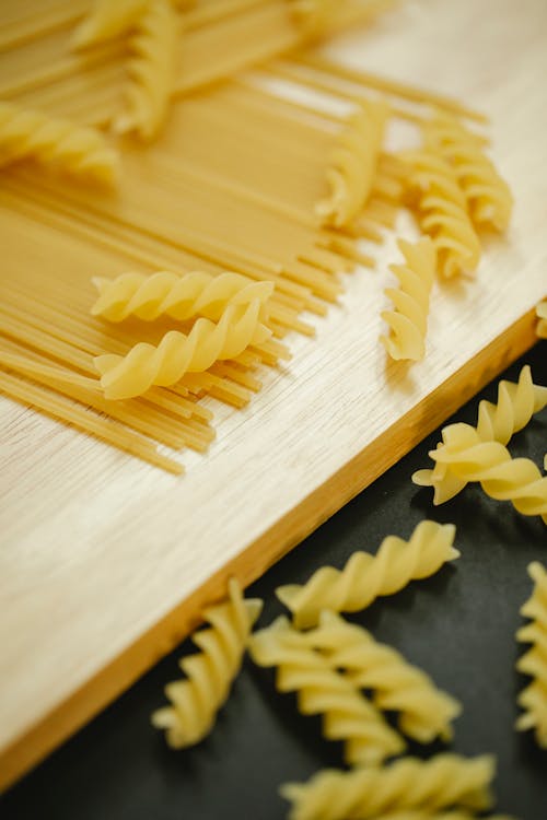 From above of raw spaghetti and fusilli pasta on wooden board for cooking process