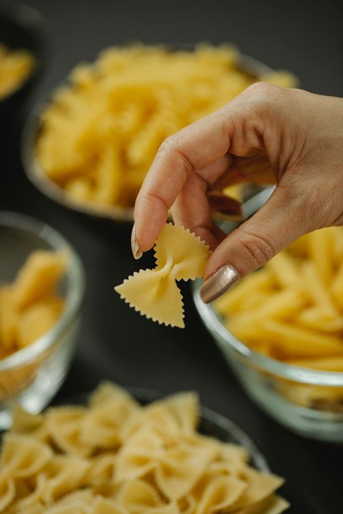 Free From above of crop anonymous female chef with piece of raw butterfly pasta Stock Photo