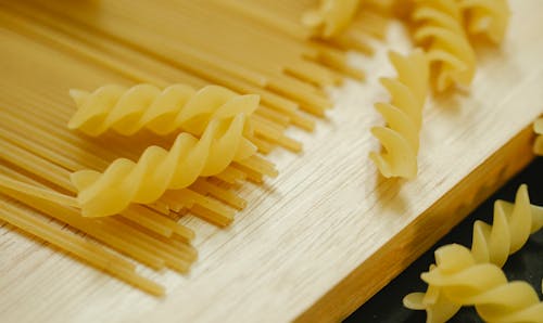 From above closeup of fusilli and spaghetti placed on wooden board for cooking dish