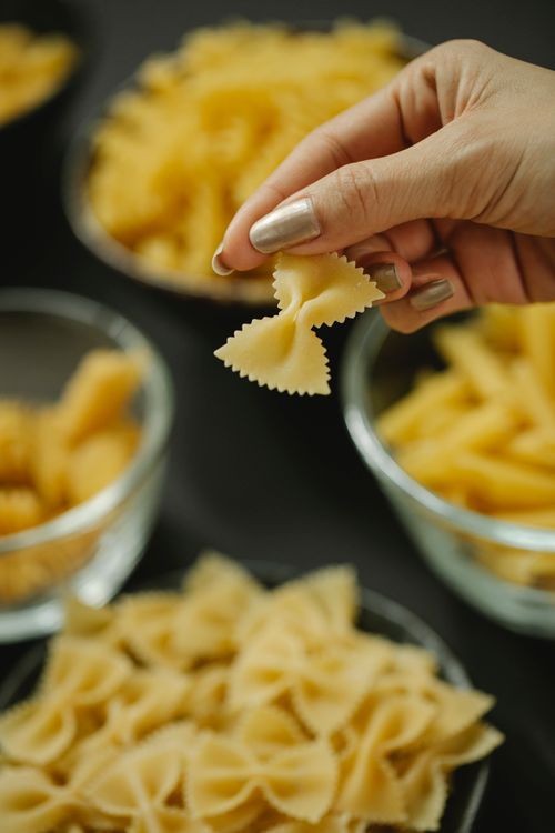 Free High angle of crop anonymous female cook holding raw farfalle under glass bowls of pasta Stock Photo