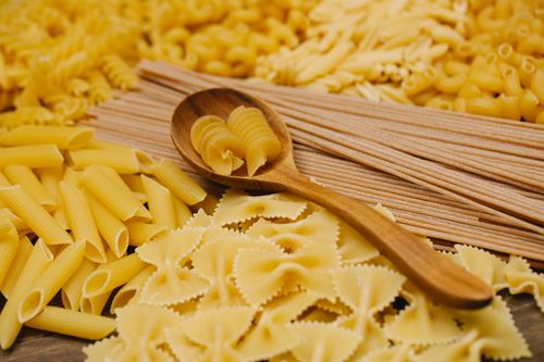 Free From above of various types of uncooked pasta including spaghetti penne and farfalle with wooden spoon Stock Photo