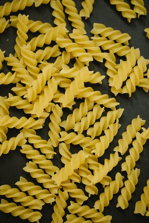 From above of pile of raw fusilli pasta scattered on black table before cooking in kitchen