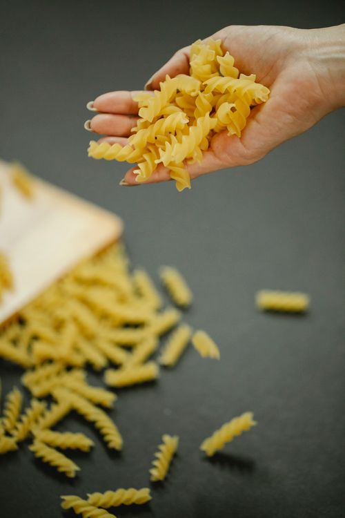 Free From above of crop unrecognizable female holding handful of fresh raw fusilli pasta over black table in kitchen Stock Photo