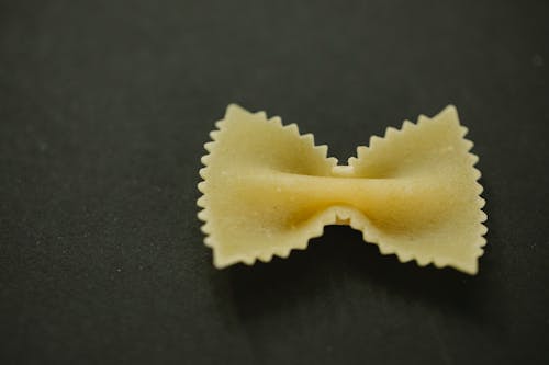 High angle closeup of piece of raw farfalle pasta placed on gray tabletop in kitchen
