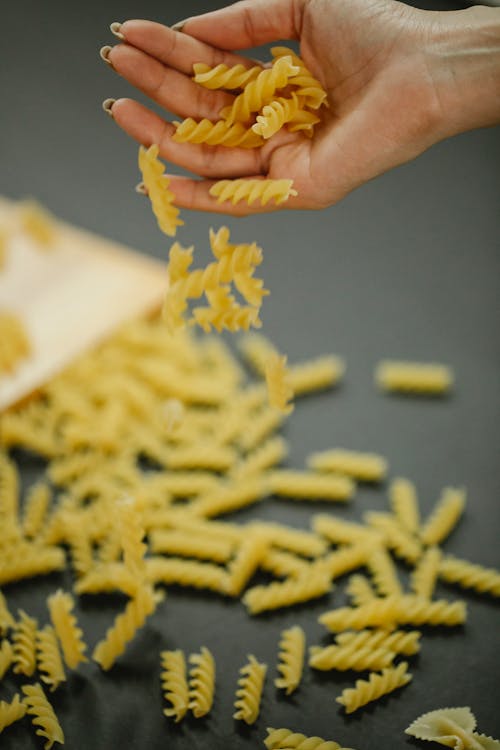 Unrecognizable woman scattering raw pasta pieces on table
