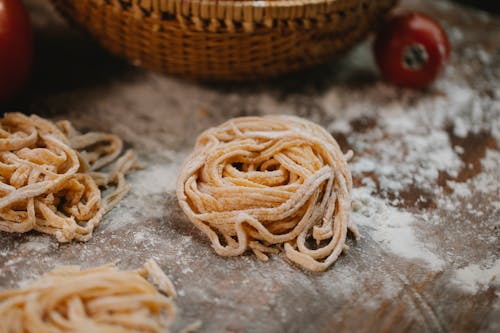Free From above nests of fresh homemade uncooked spaghetti placed on wooden table with scattered flour in kitchen Stock Photo