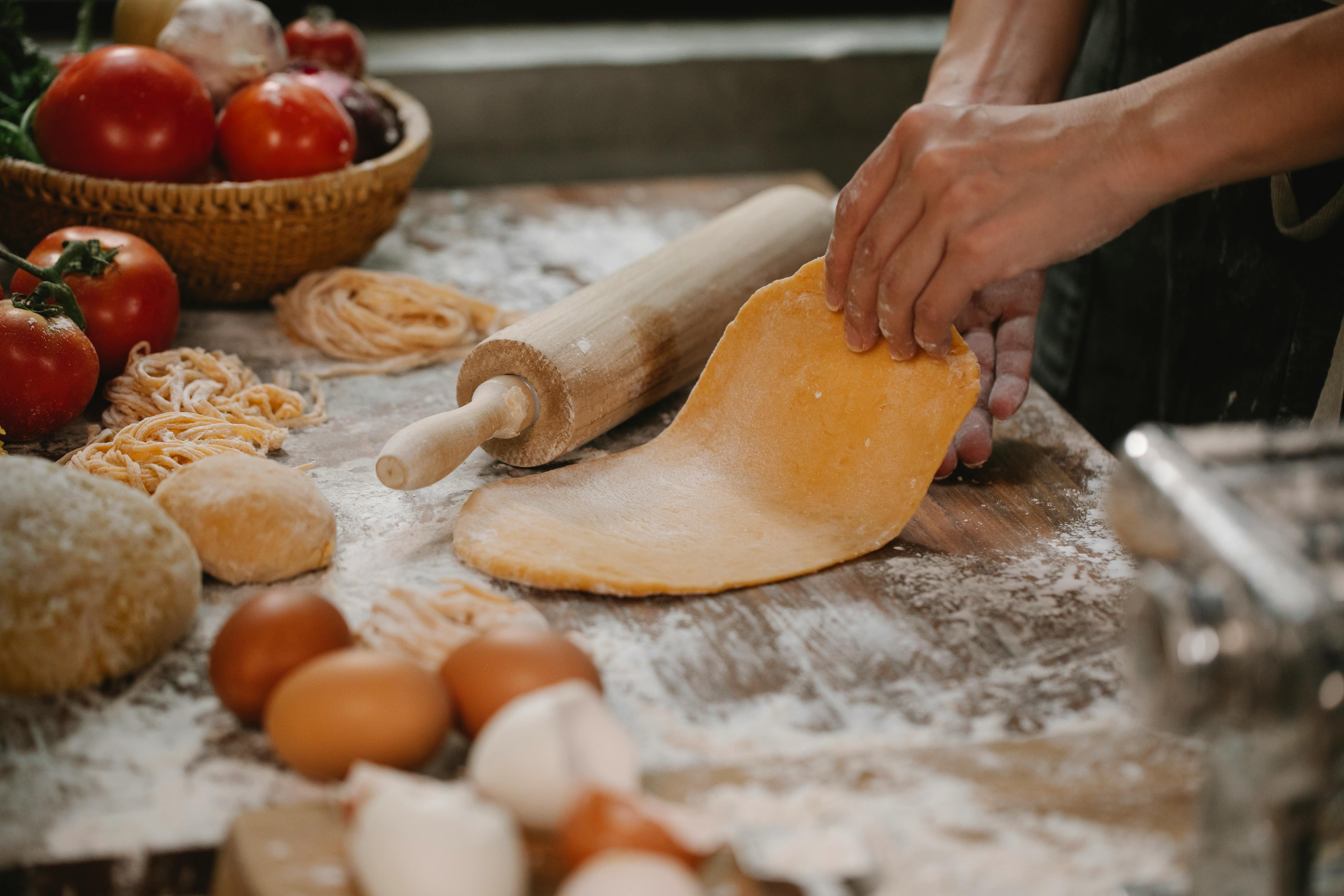 anonymous woman making dough for spaghetti standing at table with vegetables and eggs