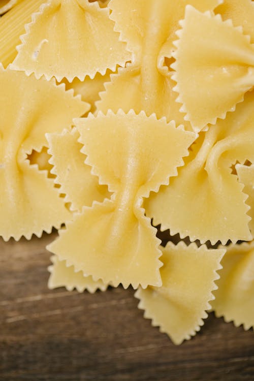 Top view of raw homemade farfalle pasta pieces scattered on wooden table in kitchen