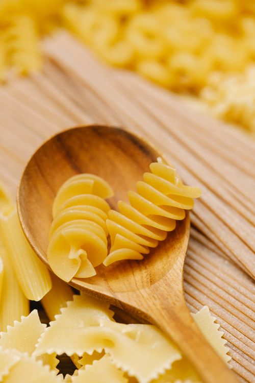 Free From above of pieces of raw rotini pasta in wooden spoon placed on table with penne and farfalle in kitchen Stock Photo