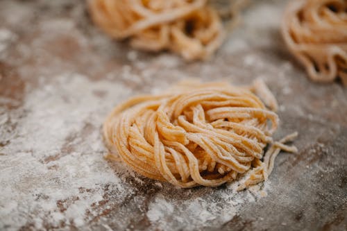 From above nest of cut uncooked spaghetti dough with flour placed on wooden table in kitchen