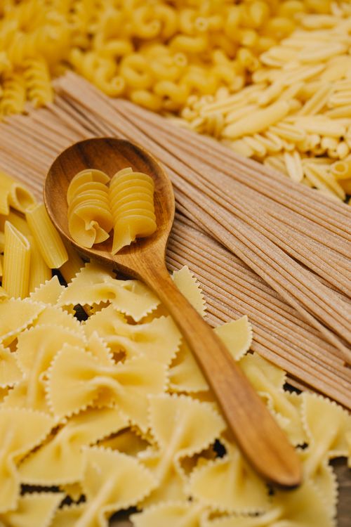 Free From above of uncooked spiral pasta in timber spoon among farfalle and different types of macaroni Stock Photo
