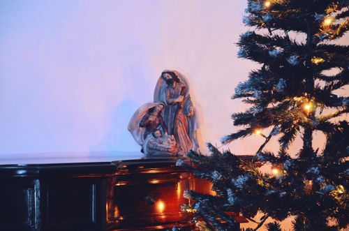 Free Warm Christmas setup featuring a nativity scene and a decorated tree with lights on a wooden table. Stock Photo