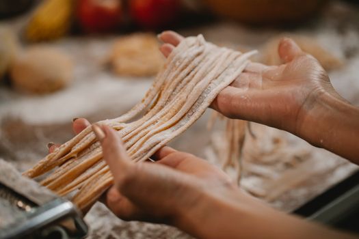 Crop anonymous female producing spaghetti with pasta cutter on blurred background of table