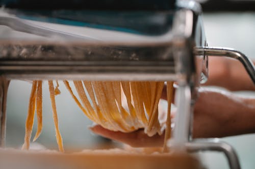 Crop anonymous female making fresh thin noodle while cutting dough in pasta machine