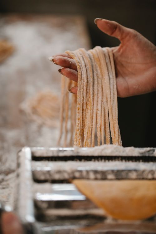 Free Crop anonymous female with spaghetti in flour prepared for cooking on blurred background Stock Photo