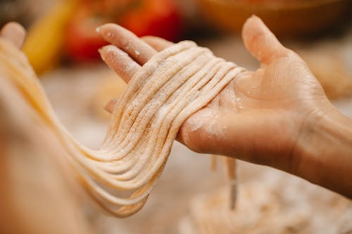 Crop anonymous female showing fresh uncooked spaghetti with flour in hands on blurred background