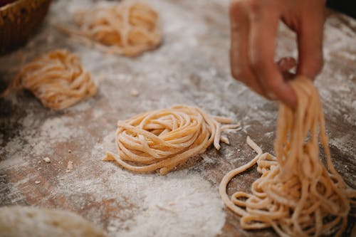 From above crop anonymous chef forming raw pasta nests on table covered with flour in kitchen