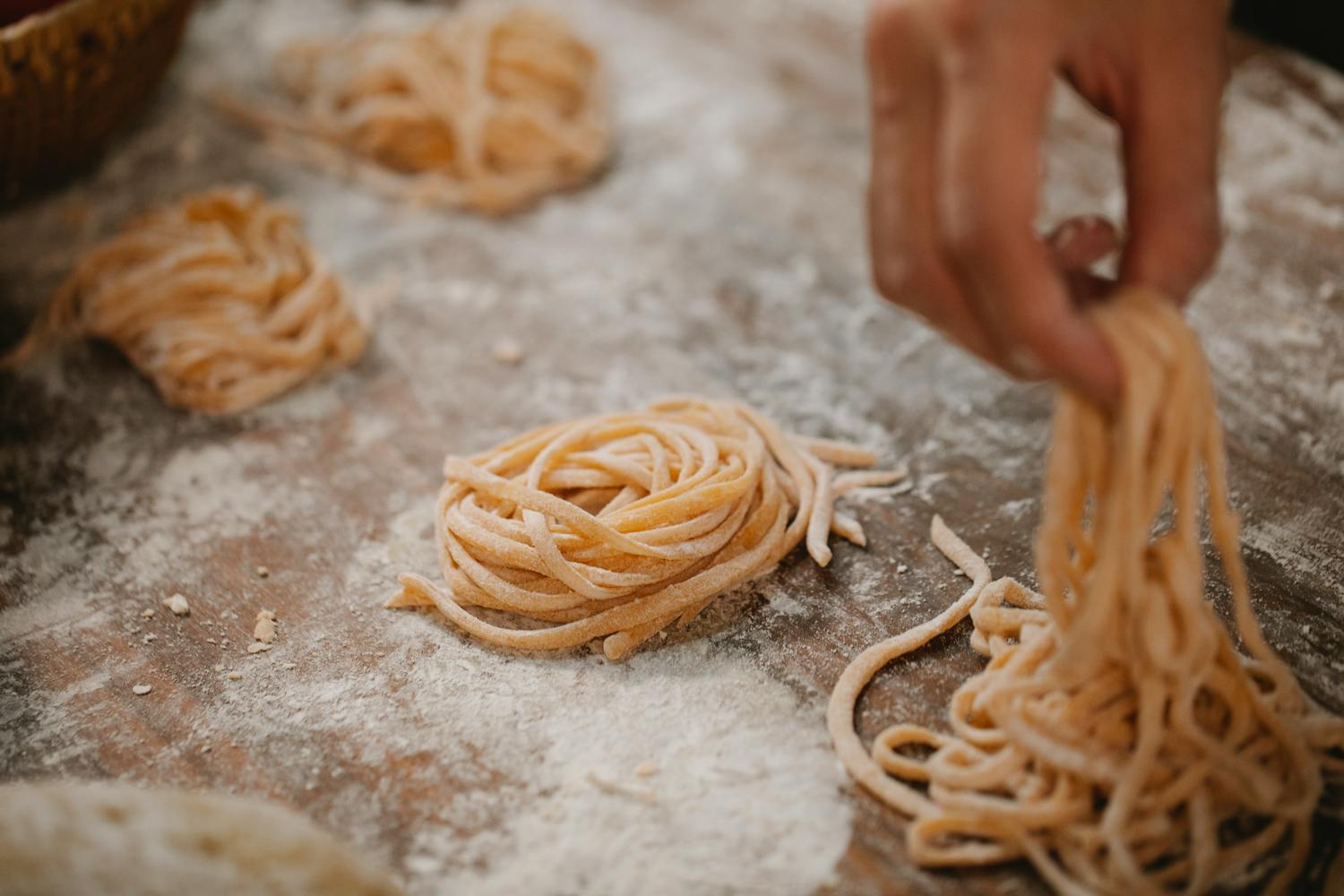Chef forming raw pasta nests on table covered with flour