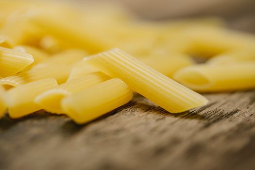 Selective focus of uncooked traditional Italian penne pasta scattered on wooden table in modern kitchen