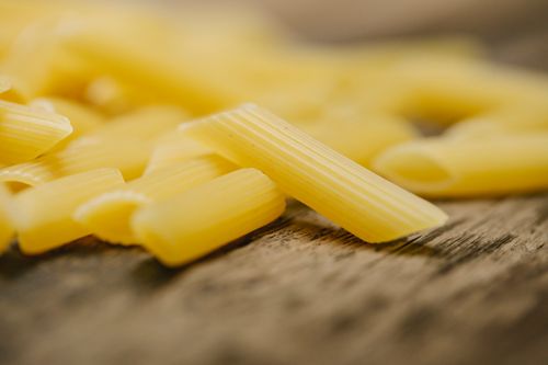 Free Selective focus of uncooked traditional Italian penne pasta scattered on wooden table in modern kitchen Stock Photo