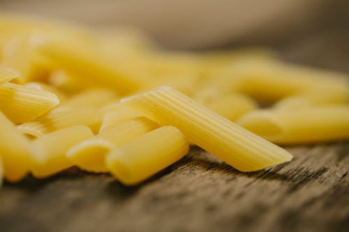 Composition of raw traditional Italian penne pasta scattered on wooden table in light kitchen