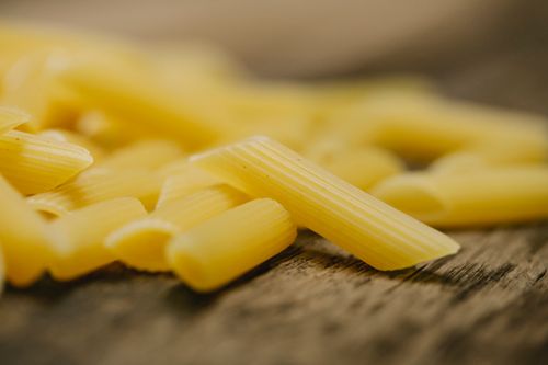 Free Composition of raw traditional Italian penne pasta scattered on wooden table in light kitchen Stock Photo