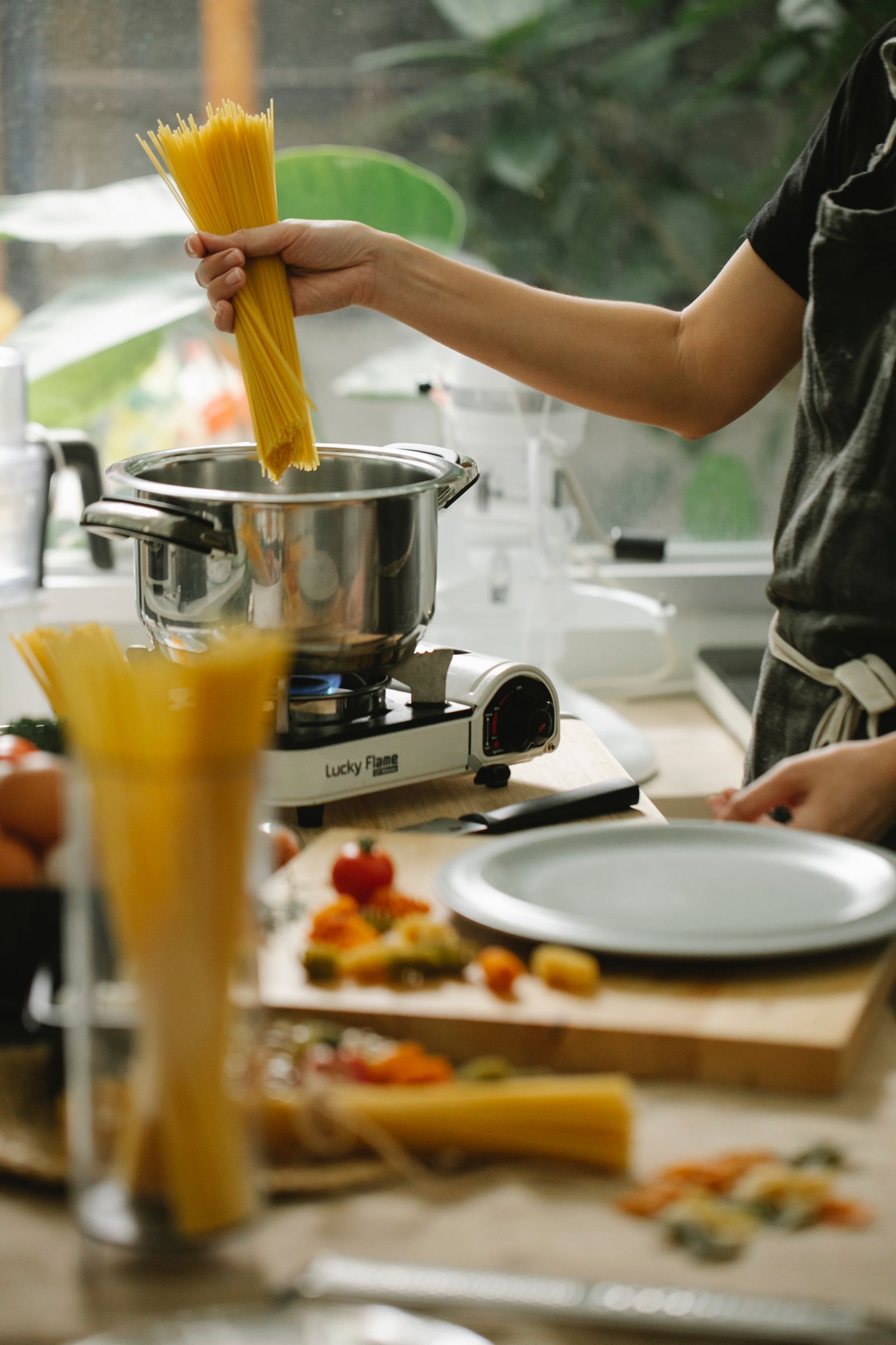 Crop unrecognizable female chef in apron putting raw spaghetti into saucepan on stove while cooking in contemporary light kitchen