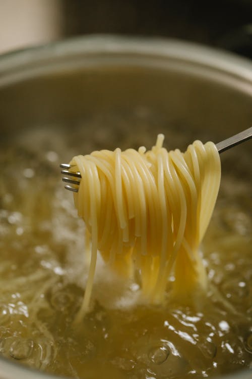Spaghetti spun on fork above boiling water in saucepan