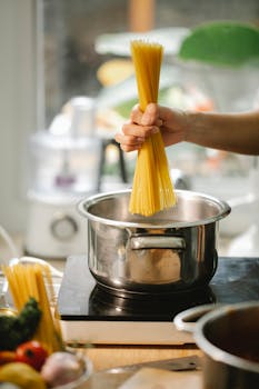 A hand preparing spaghetti pasta in a pot on the stove in a modern kitchen.