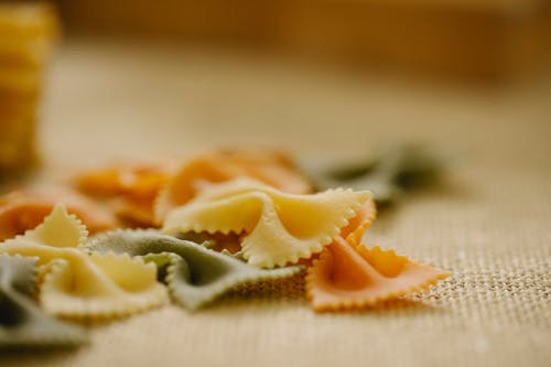 Composition of uncooked multicolored Italian farfalle pasta scattered on table in light kitchen