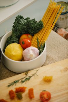 High angle composition of fresh vegetables and spaghetti in bowl placed on table near cutting board in kitchen