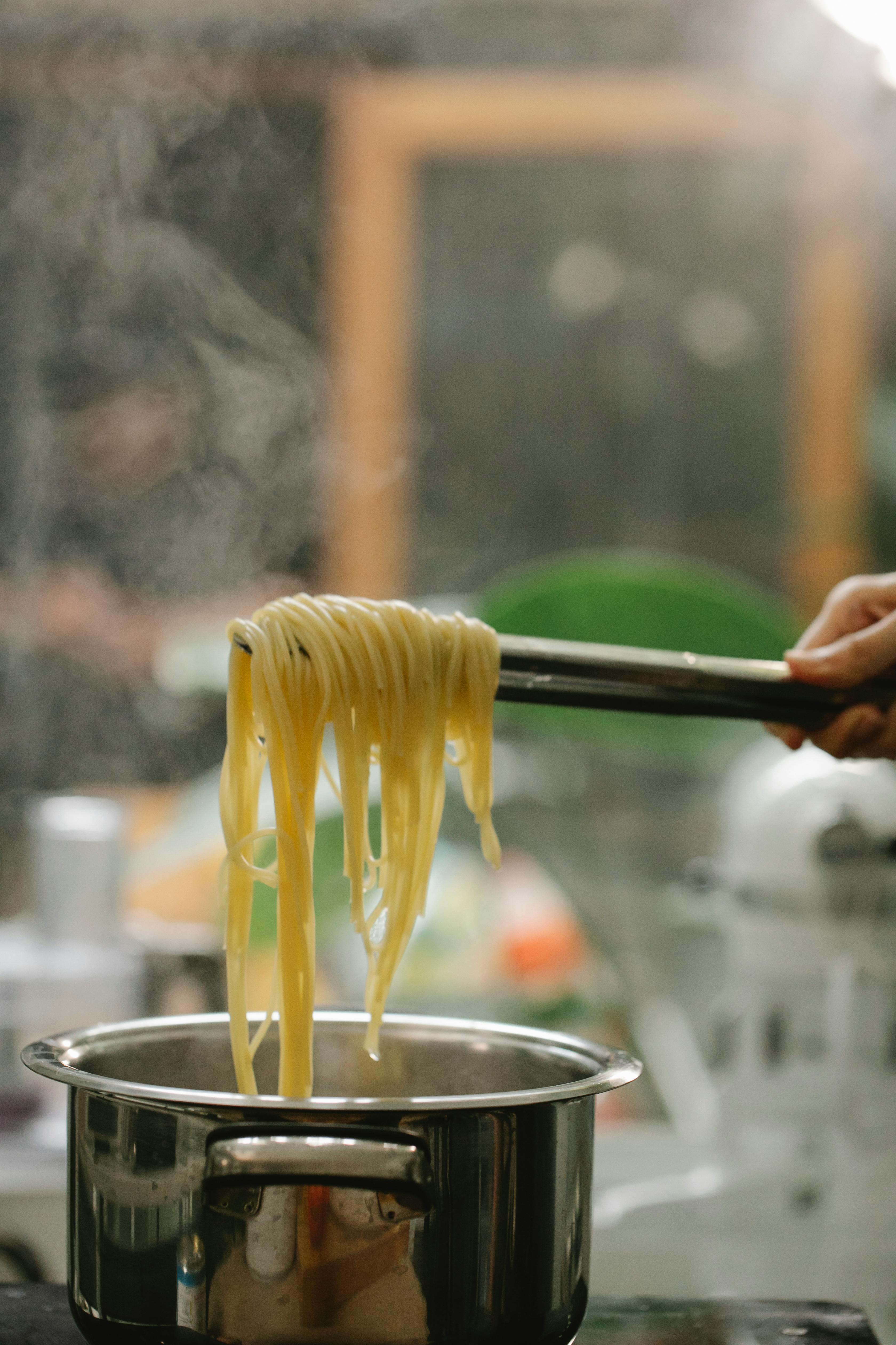 crop faceless chef picking cooked spaghetti with tongs
