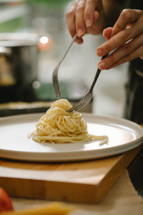 Crop unrecognizable chef serving delicious spaghetti on plate
