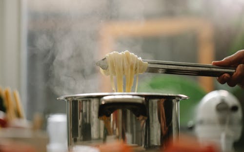 Low angle of crop anonymous chef taking spaghetti from pan with boiling steaming water
