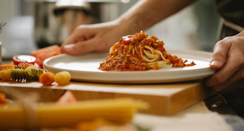 Cook taking plate with pasta Bolognese in kitchen