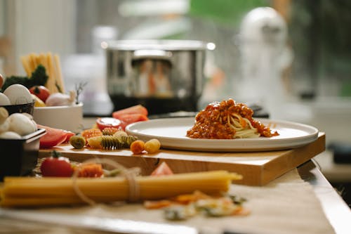 Appetizing homemade pasta with sauce on plate placed on wooden board in kitchen with different ingredients