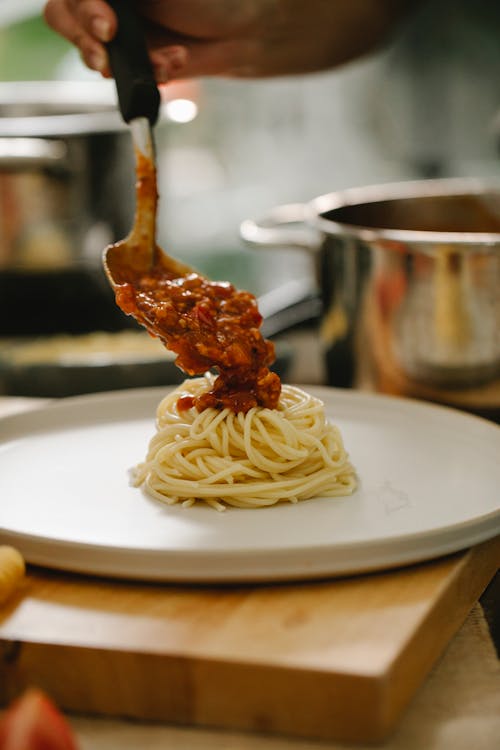 Crop faceless chef adding fresh Bolognese sauce to spaghetti