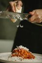 Crop anonymous female chef grating fresh cheese on yummy spaghetti with tomato sauce on white plate