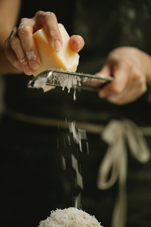 Crop faceless cook grating tasty cheese on dish