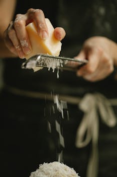 Hands grating cheese for a dish; culinary preparation with focus on detail.