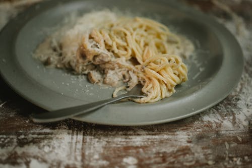 Fork placed on plate with yummy fresh spaghetti pasta in cream mushroom sauce served on shabby table