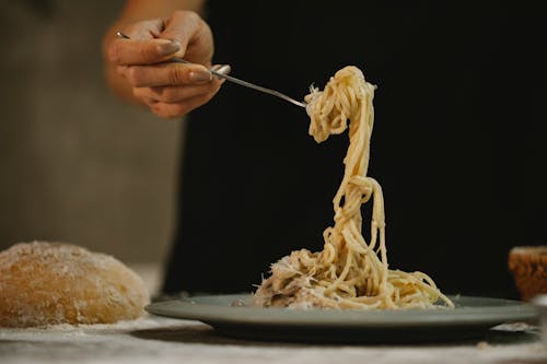 Crop unrecognizable woman eating spaghetti in cream sauce