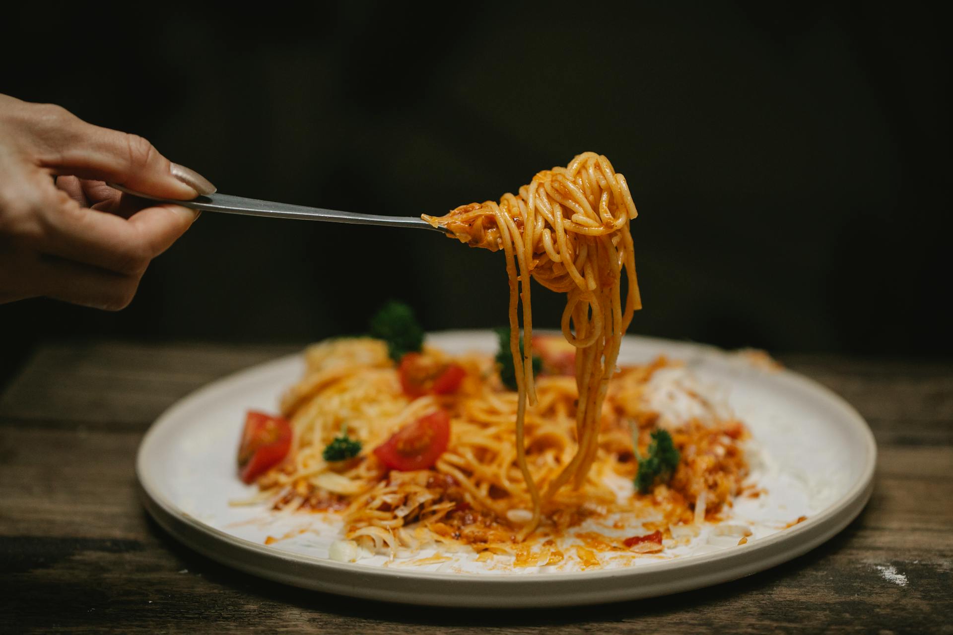 Crop anonymous female with fork enjoying yummy Bolognese pasta garnished with cherry tomatoes and parsley