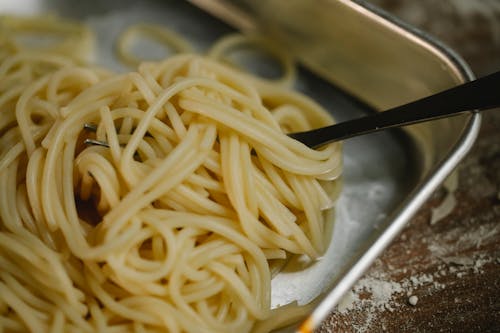Cooked spaghetti and fork placed in steel bowl