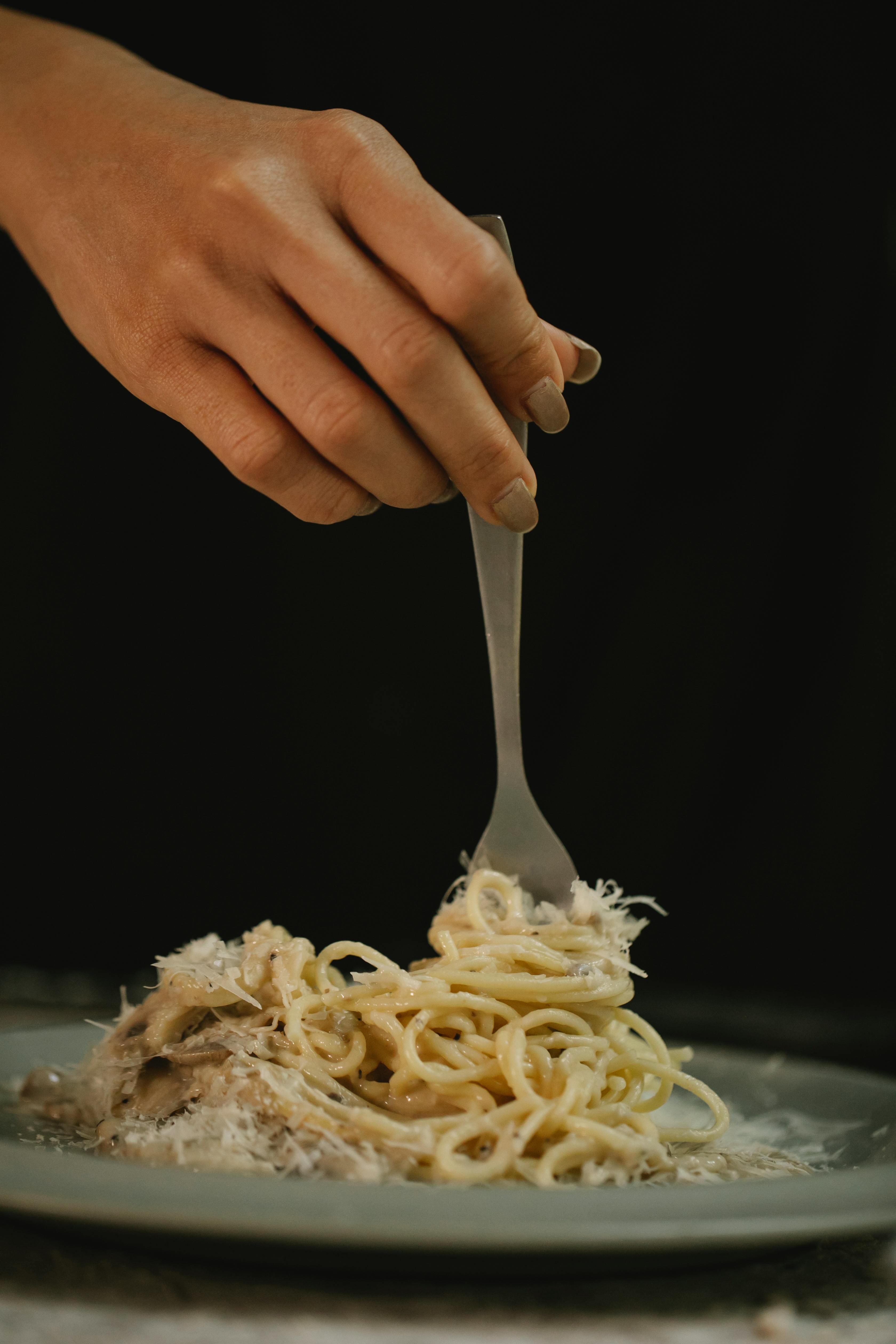 crop unrecognizable woman eating delicious pasta in cream sauce