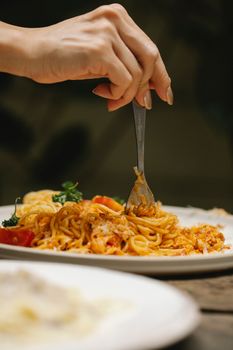 Crop anonymous female rolling yummy Bolognese pasta on fork while dining in restaurant
